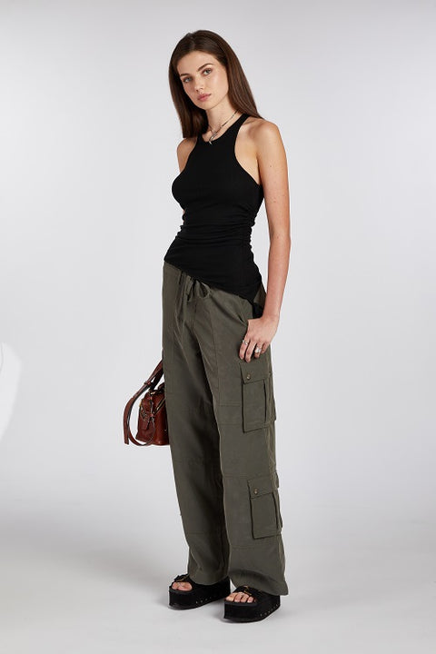 Side view of the black racerback tank top showing its asymmetric hemline paired with a green cargo pant. The soft, stretchy fabric drapes beautifully for a flattering fit.