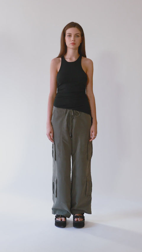 360-degree view of a chic and elegant black racerback tank top with an asymmetric hem, paired with olive green cargo pants. Made from soft, stretchy, and sustainable ribbed knit fabric for a sexy yet versatile fit. The full spin showcases the tank's flattering drape, open-back detail, and styling versatility—from sleek and fitted to relaxed and effortless.