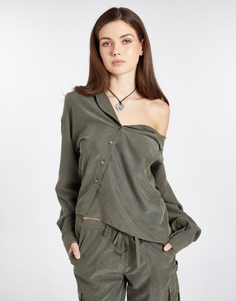 Modern and effortlessly cool one-shoulder asymmetric button-up blouse in olive green, crafted from buttery soft TENCEL modal woven fabric, shown as part of a matching set with baggy olive green cargo pants in SoHo, NYC. Paired with black strappy sandals, this sustainable, drapey top embodies minimal style and elevated essentials, offering a relaxed yet flattering fit. With its earthy, neutral tone, this versatile piece is perfect for the modern city hippie—chic, free-spirited, and effortlessly stylish.