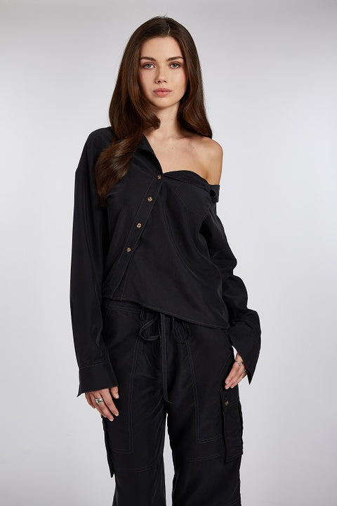 Close up of modern and elegant one-shoulder asymmetric button-up blouse in black, crafted from buttery soft TENCEL modal woven fabric, shown paired with heels and flip-flop heels. This sustainable, drapey top offers a flattering fit with a relaxed yet subtly sexy silhouette. Designed for versatility, it resists wrinkles and transitions effortlessly from work to dinner, errands to events—perfect for any occasion.