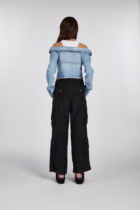 Back of off-shoulder denim jacket with a built-in white ribbed racerback tank top, paired with drapey, baggy black cargo pants for an effortlessly cool look. Crafted from premium Italian denim in a light wash, this slouchy yet elegant 2-in-1 top features a slightly cropped fit, making it the perfect transitional outfit. Designed for versatility, it’s ideal for summer nights or layering through the seasons.