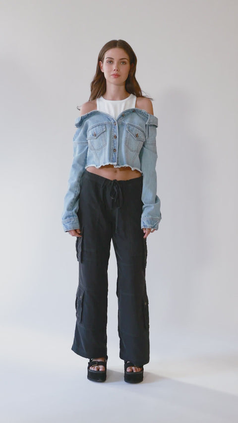 360-degree view of an off-shoulder denim jacket with a built-in white ribbed racerback tank top. Crafted from premium Italian denim in a light wash, this slouchy yet elegant 2-in-1 top features a slightly cropped fit and effortlessly cool silhouette. The full rotation showcases its unique structure, relaxed drape, and transitional versatility—perfect for pairing with baggy cargo pants or styling from day to night."