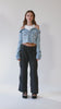 360-degree view of an off-shoulder denim jacket with a built-in white ribbed racerback tank top. Crafted from premium Italian denim in a light wash, this slouchy yet elegant 2-in-1 top features a slightly cropped fit and effortlessly cool silhouette. The full rotation showcases its unique structure, relaxed drape, and transitional versatility—perfect for pairing with baggy cargo pants or styling from day to night."