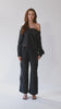 360-degree video of an elegant one-shoulder asymmetric button-up blouse in black, crafted from buttery soft TENCEL modal woven fabric, shown as part of a matching set with baggy black cargo pants in SoHo, NYC. Paired with heels and flip-flop heels, this sustainable, drapey top embodies minimal style and elevated essentials, offering a flattering fit with a relaxed yet subtly sexy silhouette. Designed for versatility, it resists wrinkles and transitions effortlessly from work to dinner, errands to ev